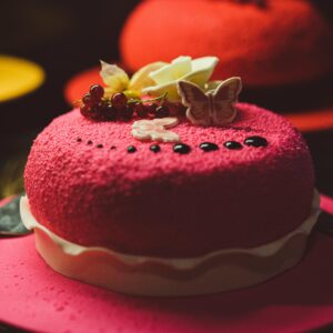 Close-up of a vibrant red velvet cake with berry toppings and a butterfly decoration on a red plate.