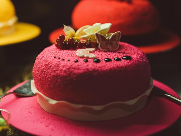 Close-up of a vibrant red velvet cake with berry toppings and a butterfly decoration on a red plate.